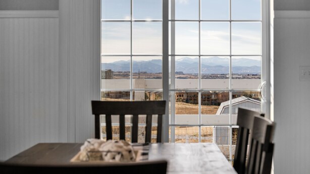 Uma área de refeições com mesa e cadeiras, uma janela com vista para montanhas e um rio.