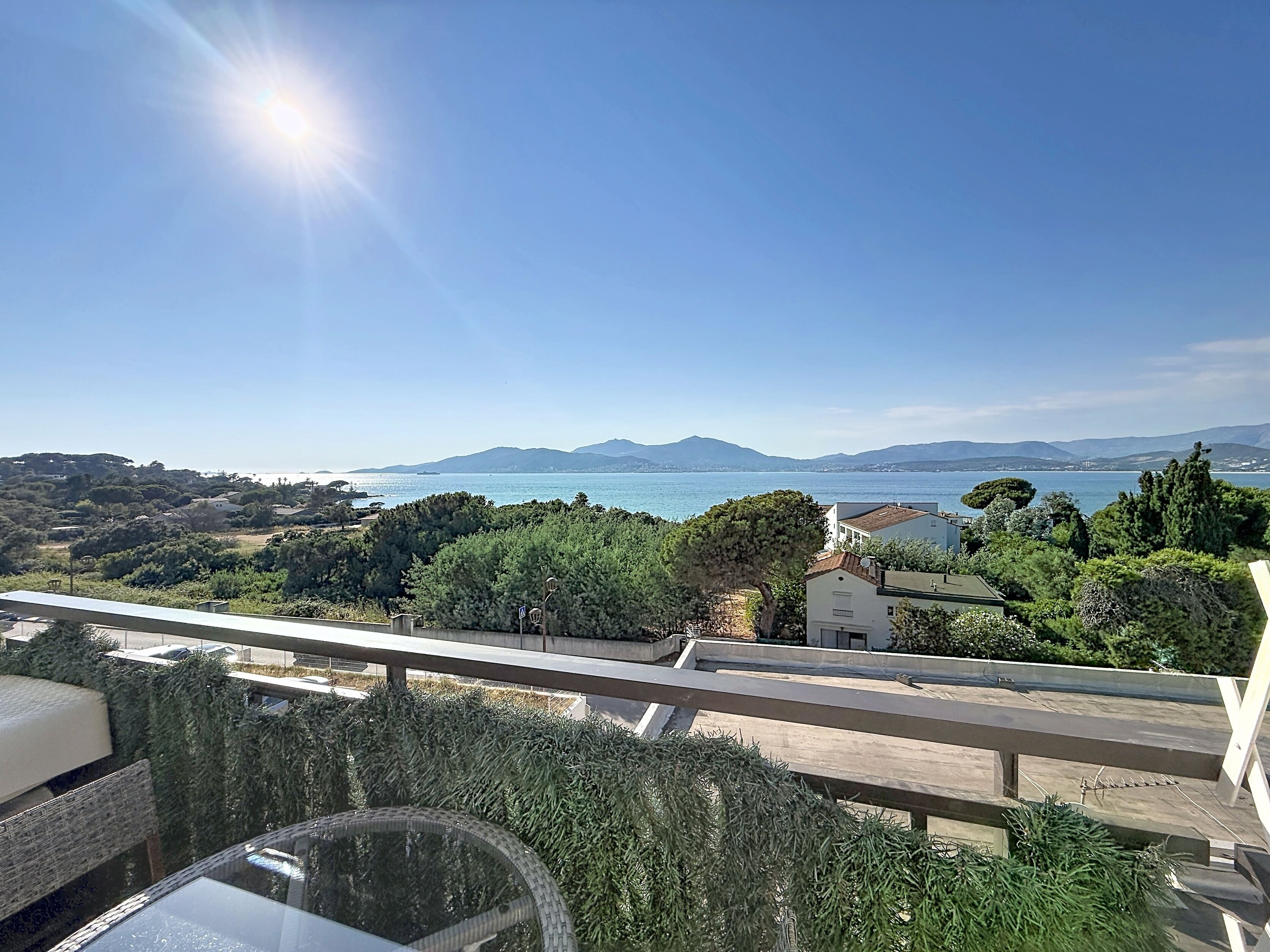 A balcony with a view of a coastal landscape, including trees and a distant body of water.