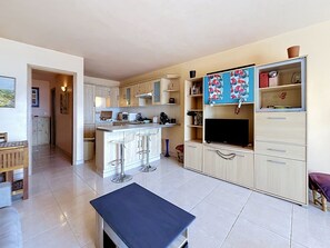 A modern kitchen with a central island, bar stools, a dining area with a table, and a living area with a TV and shelving. - Exceptional view of the sunsets.  (Grosseto-Prugna)