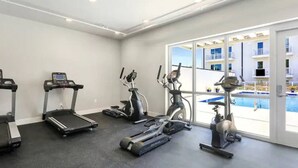 A gym with treadmills, elliptical machines, and a stationary bike, with a pool visible through the windows.