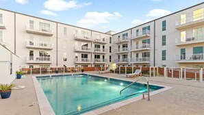 A modern apartment building with a swimming pool, outdoor seating, and balconies.