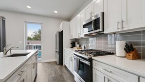 A modern kitchen with white cabinets, stainless steel appliances, and a large window.