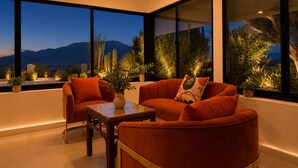 A modern interior with a sofa and armchair, a small table, and large windows with a view of mountains.