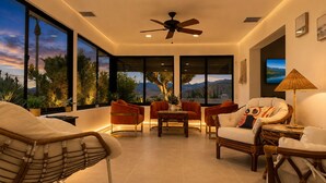 A modern living room with large windows, a ceiling fan, and a view of the outdoors.