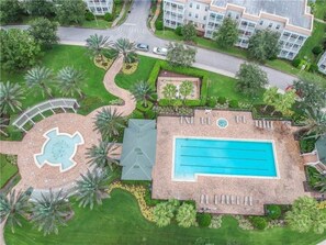 An aerial view of a residential area with a swimming pool, palm trees, and a circular garden with a fountain.
