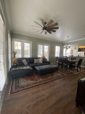 A spacious living room with a dark-colored sofa, a patterned rug, and a ceiling fan.