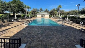 Ein Swimmingpool mit Liegestühlen und Sonnenschirmen, umgeben von Palmen und einem überdachten Sitzbereich.