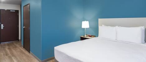 Una habitación de hotel con una cama grande, una mesita de noche con una lámpara y una puerta.