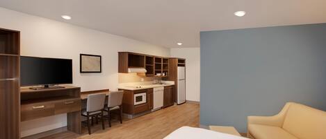 A compact hotel room with a kitchenette, a bed, a TV, and a seating area.