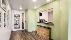 Un couloir doté d’un plancher en bois, une porte en verre donnant sur une pièce, un meuble en bois et un miroir fixé au mur.