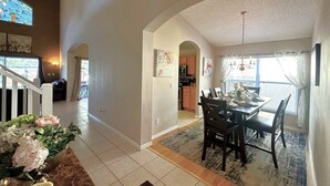 A spacious living area with a dining table set for four, a kitchen in the background, and a staircase leading to another level. - Comfort Single Home with BBQ, Private Pool & Hot Tub (Kissimmee)