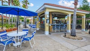 An outdoor patio area with blue and white striped chairs and tables, a covered seating area, and a clock on the wall. - Comfort Single Home with BBQ, Private Pool & Hot Tub (Kissimmee)