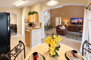 A spacious living area with a dining table, chairs, a sofa, and a television displaying 'Day Family.' - Comfort Single Home with BBQ, Private Pool & Hot Tub (Kissimmee)