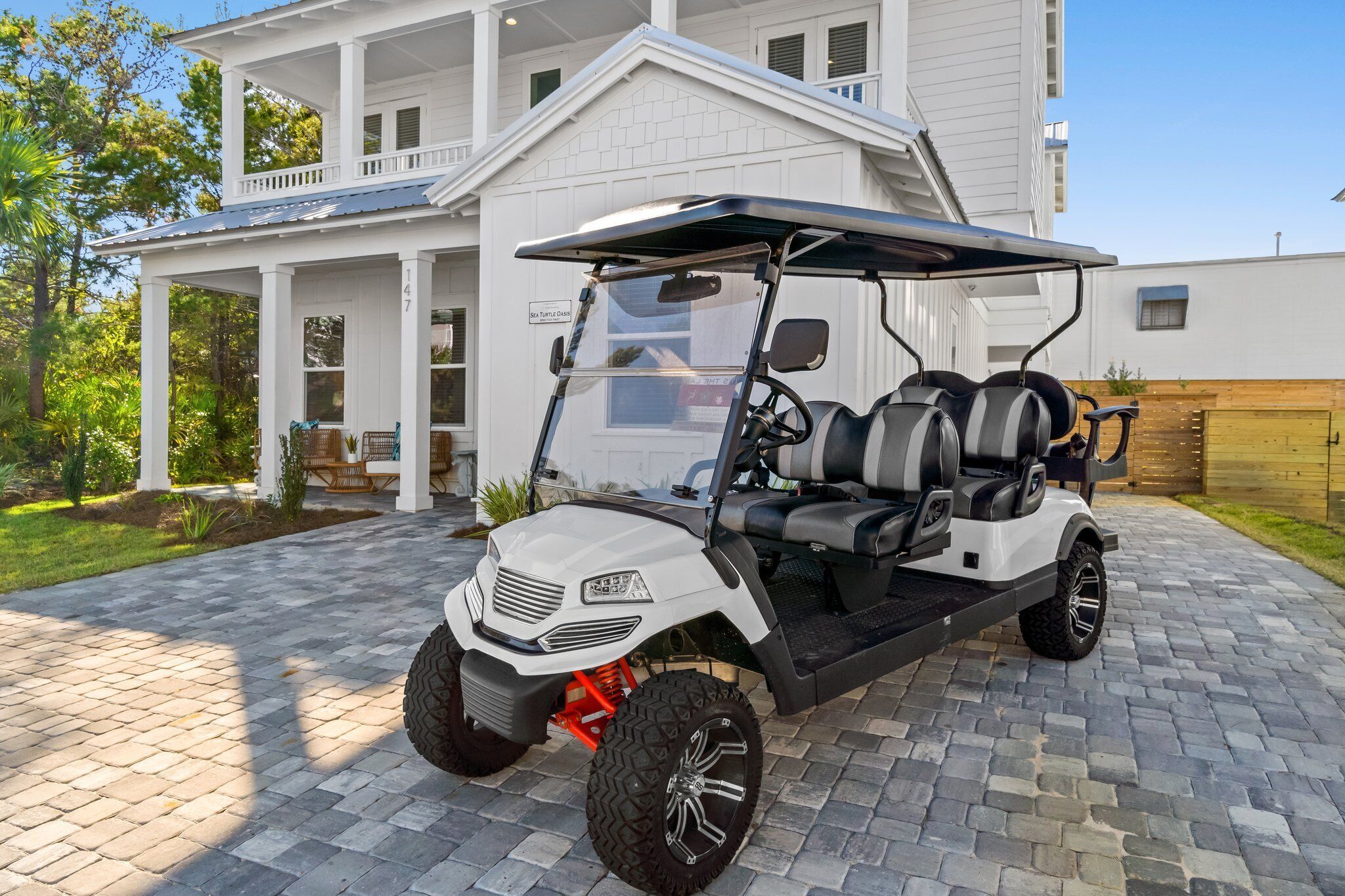 Een golfkarretje geparkeerd op een geplaveid pad voor een wit huis met een veranda.