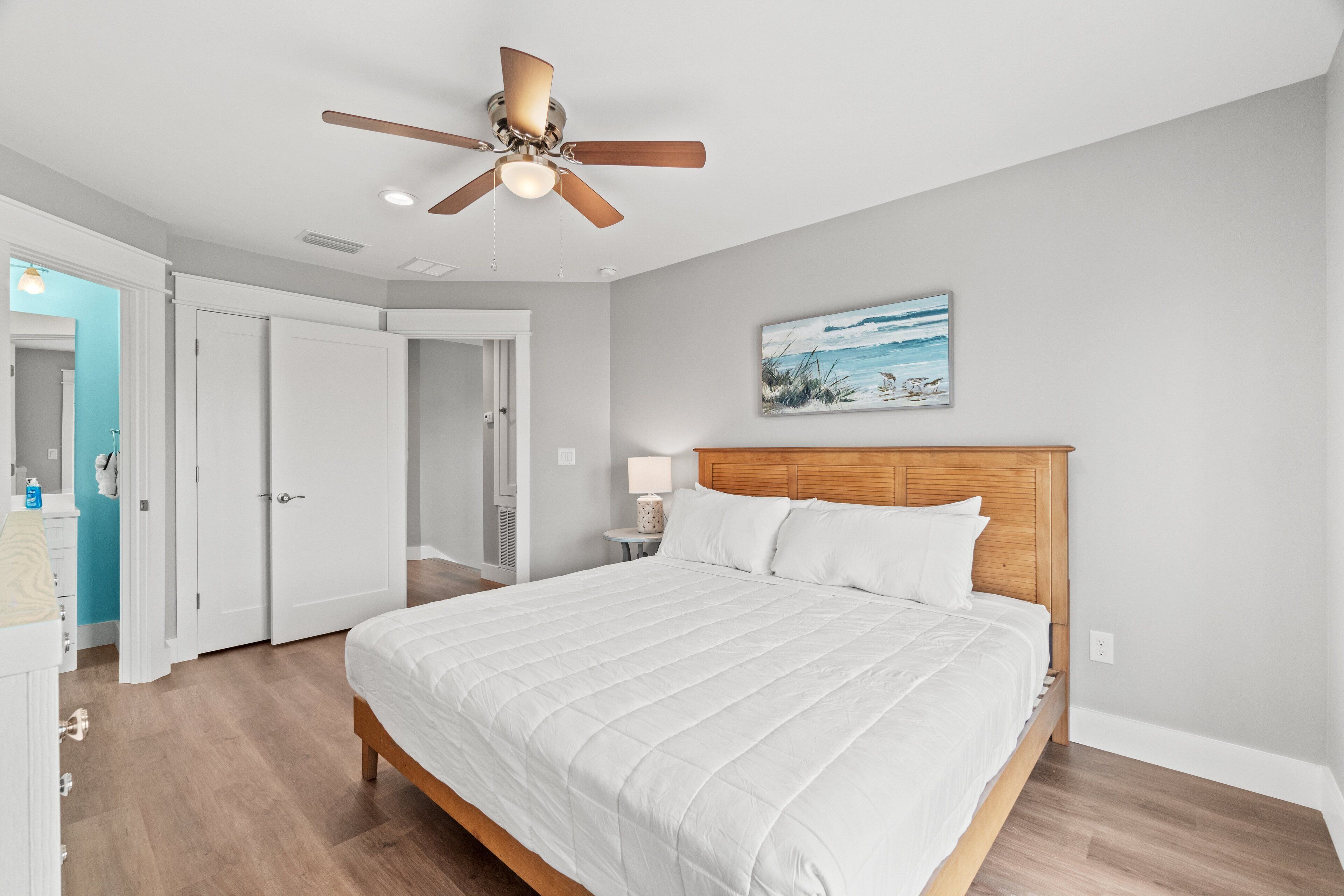 A bedroom with a large bed, wooden headboard, a ceiling fan, and a painting on the wall.