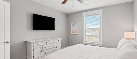 Una camera da letto con un letto, una cassettiera, una ventola a soffitto, un televisore, una finestra e una porta.