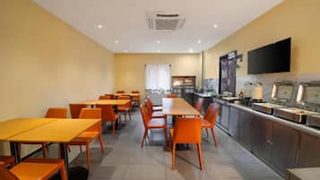 A dining area with tables and chairs, a kitchen area with appliances, and a television mounted on the wall.