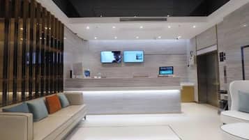 A modern reception area with a reception desk, two monitors, a sofa, and a chair.