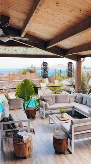 Un espacio de estar al aire libre cubierto con piscina, muebles de madera y vistas al océano.