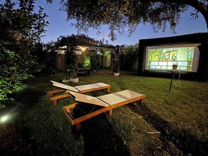 An outdoor seating area with wooden loungers and a projection screen displaying a video game.