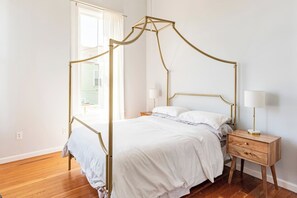 Une chambre avec un lit à baldaquin, une table de chevet avec une lampe et une fenêtre avec des rideaux.