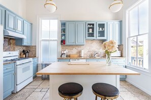 A kitchen with light blue cabinets, a central island with stools, a stove, and a coffee maker. - Renovated Historic House minutes from SF! (Oakland)