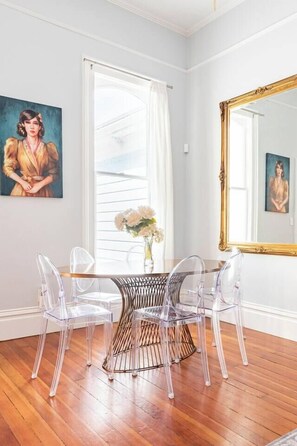 A room with a dining table, clear chairs, a vase with flowers, a large mirror, and artwork on the walls. - Renovated Historic House minutes from SF! (Oakland)