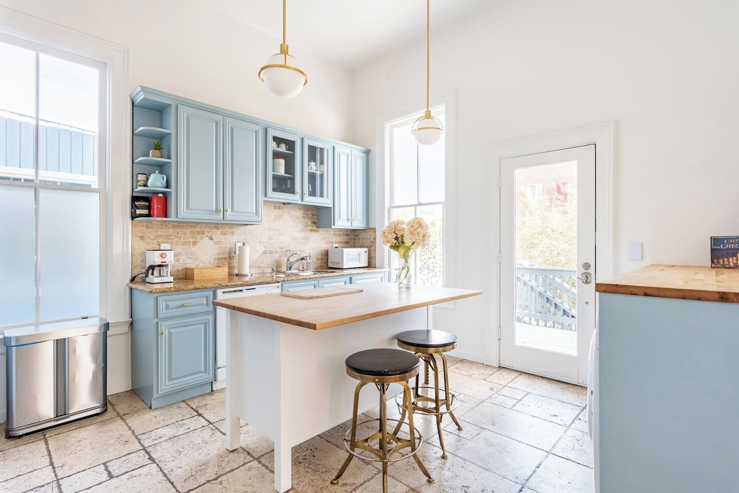 A modern kitchen with light blue cabinets, a central island with stools, a stainless steel refrigerator, and a white microwave.