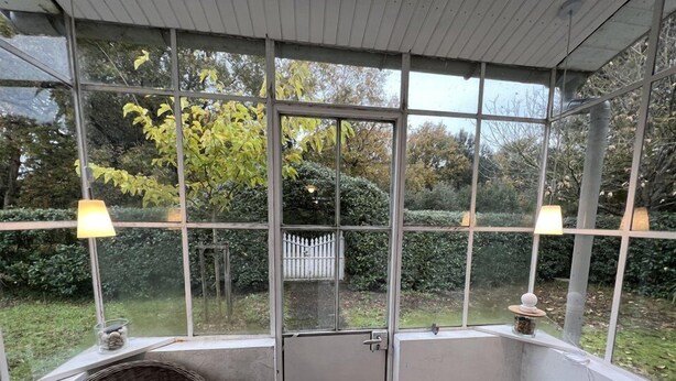 Un invernadero con una silla de mimbre, un banco y una puerta.