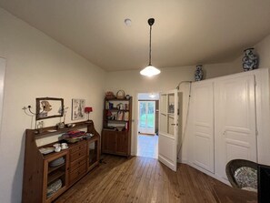 A hallway with wooden flooring, a wooden cabinet with drawers, a bookshelf, and a white wardrobe.