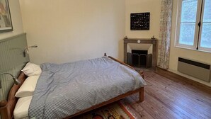 Un dormitorio con cama, sillón, chimenea y ventana.