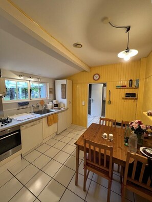 Compact kitchen with oven, sink, and window. Dining area features a table and chairs under a chandelier.