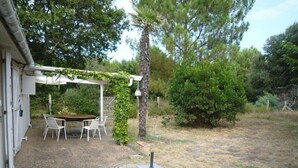 Un patio techado con mesa y sillas, rodeado de árboles y un jardín césped.
