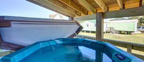 A hot tub under a wooden deck with a view of a green house in the background.
