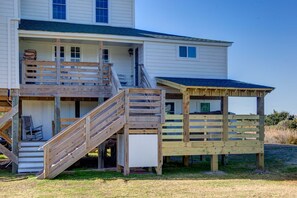 Une maison à deux étages dotée d’une terrasse en bois et d’un petit espace couvert.
