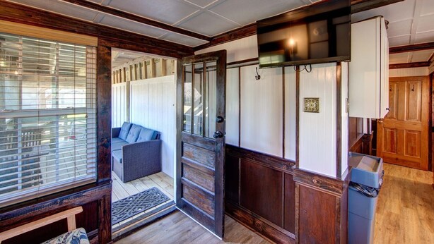 A room with a wooden door, a bench, a television, and a trash bin. - Historic suite with a private hot tub! (Avon)
