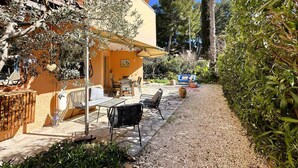 Eine Terrasse im Freien mit Tisch und Stühlen, umgeben von Olivenbäumen und einem Kiesweg.