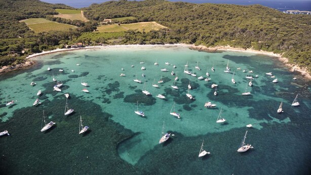 Ein Luftbild einer Küstenregion mit zahlreichen Segelbooten, die in klarem türkisblauem Wasser ankerten, umgeben von üppigen grünen Hügeln und einem Sandstrand.