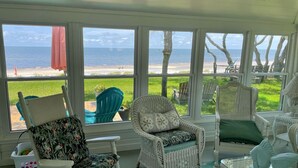 Una veranda soleggiata con mobili in vimini, ampie finestre vista spiaggia e vista sull'oceano.