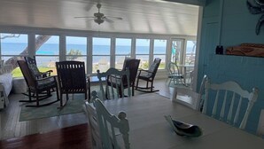 Zona pranzo con vista sull'oceano, arredi bianchi e ventilatore a soffitto.