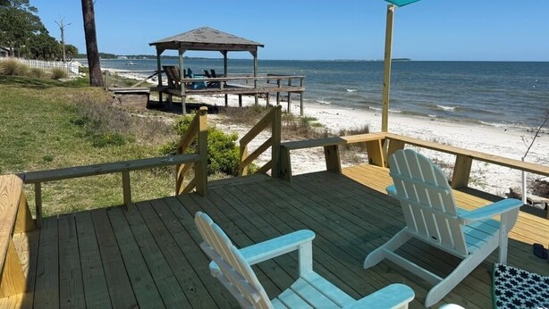 Un terrazzino in legno con poltrone Adirondack, un gazebo e vista sulla spiaggia e sull'oceano.