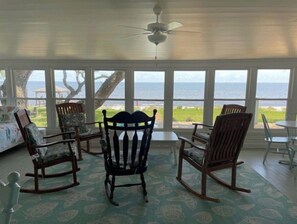 Relax in this serene sunroom with a stunning ocean view, featuring a ceiling fan, a comfortable rocking chair, and a bench.