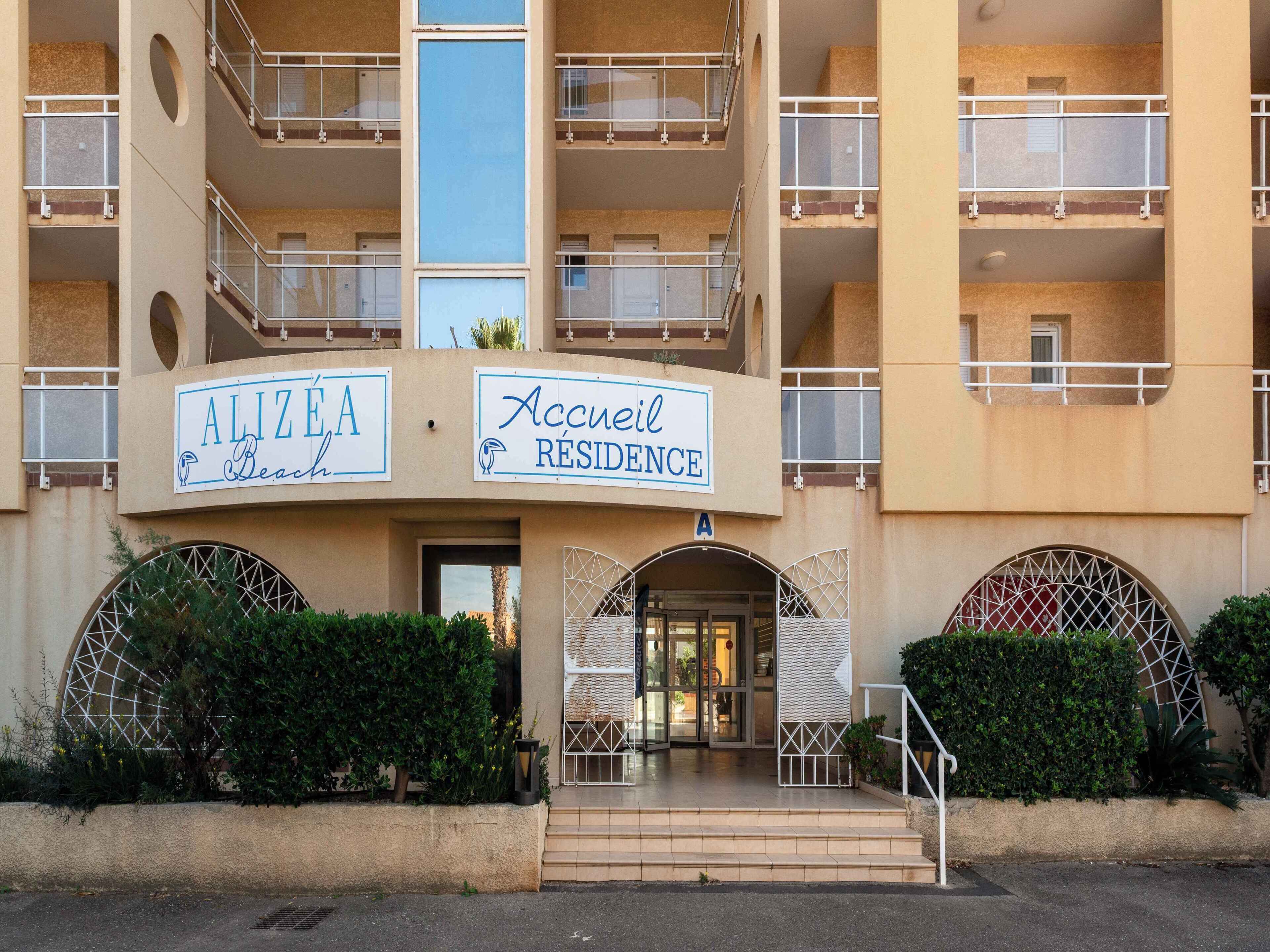 A multi-story building with balconies, a sign reading "Alizea Residence," and a gated entrance.