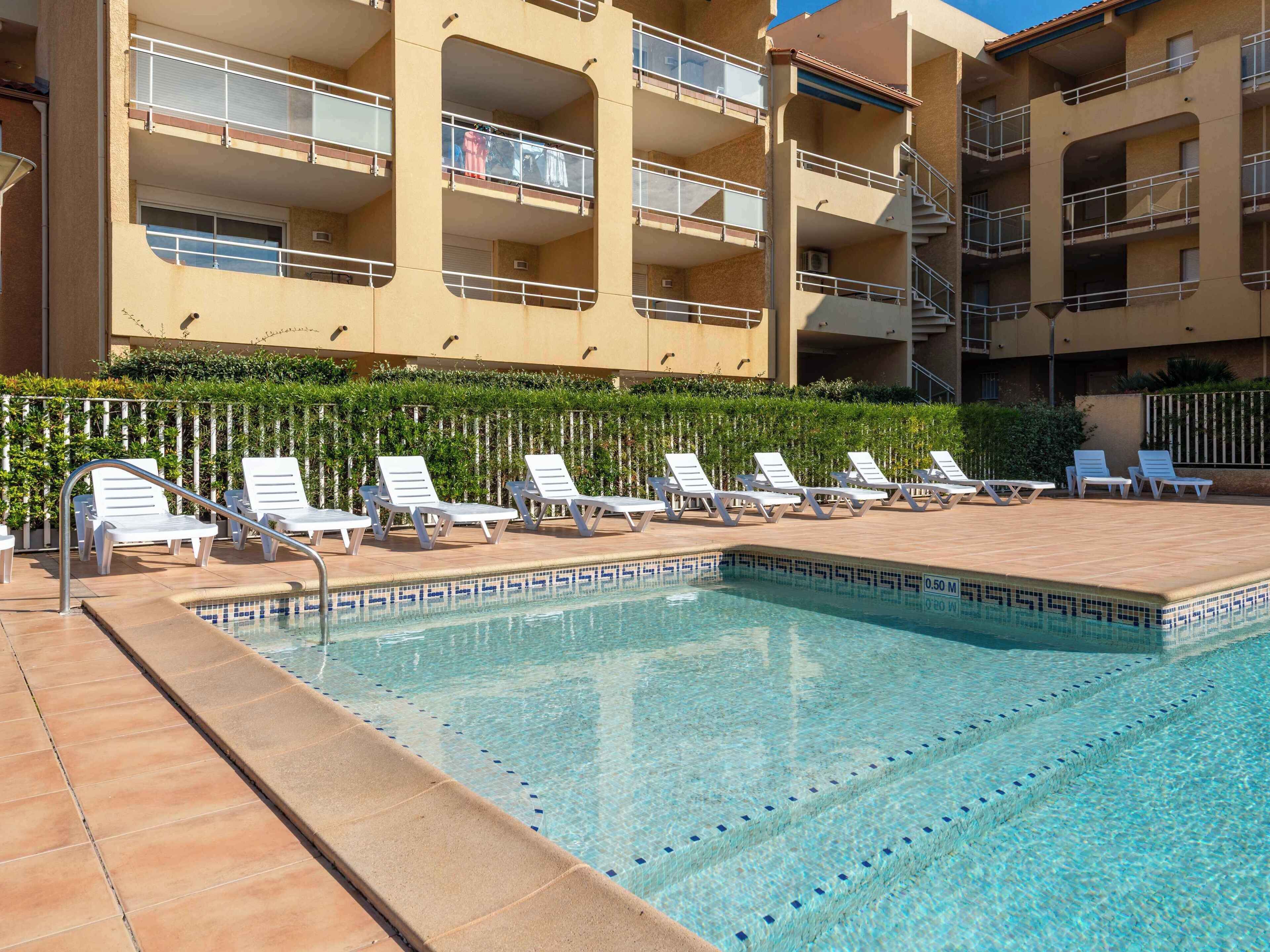 A pool area with lounge chairs and a building with balconies in the background.