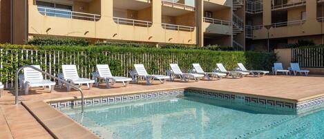 A pool area with lounge chairs and a building with balconies in the background.