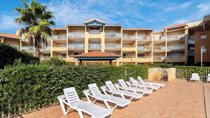 Un hôtel doté de nombreux balcons, d’un palmier et d’un espace piscine avec des chaises longues.