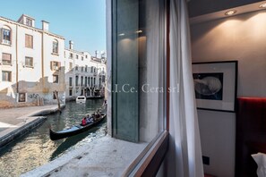 A canal view from a room with a large window, a gondola on the water, and a building with balconies.