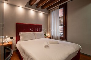 A neatly made bed with white linens, a red headboard, and a bedside table with a lamp.