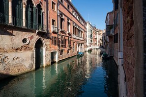 A narrow canal with buildings on either side, a bridge in the distance, and a boat in the water.