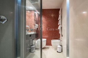 A modern bathroom with a glass shower enclosure, a white sink, a bidet, and a toilet.